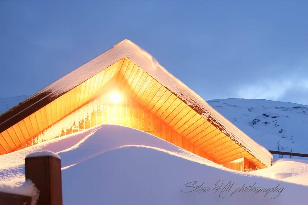 Snow-covered log cabin glowing with warm light at dusk
