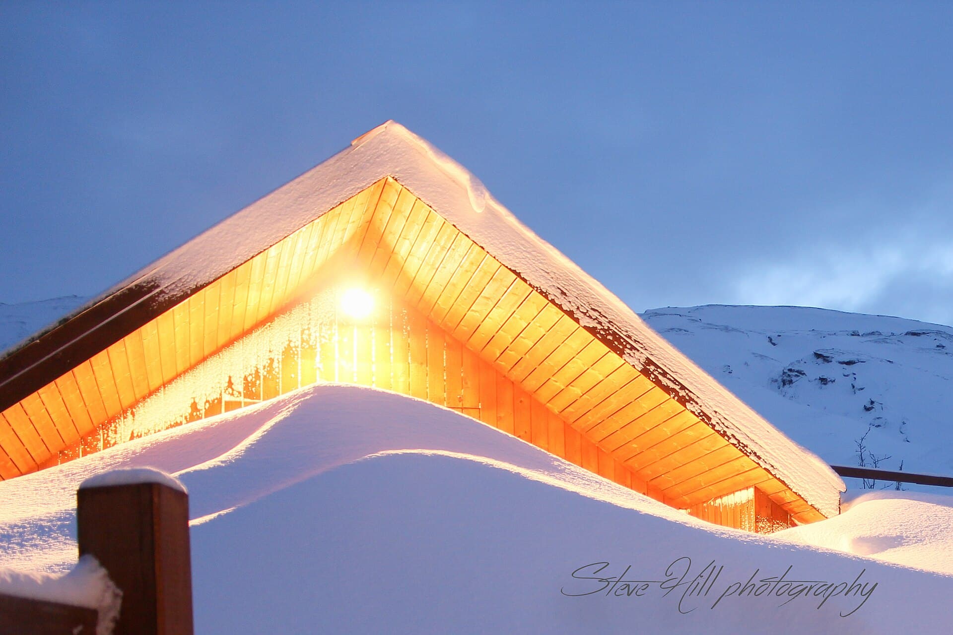 Snow-covered log cabin glowing with warm light at dusk