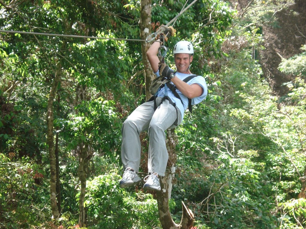 Person gliding along a zip line through a green forest canopy