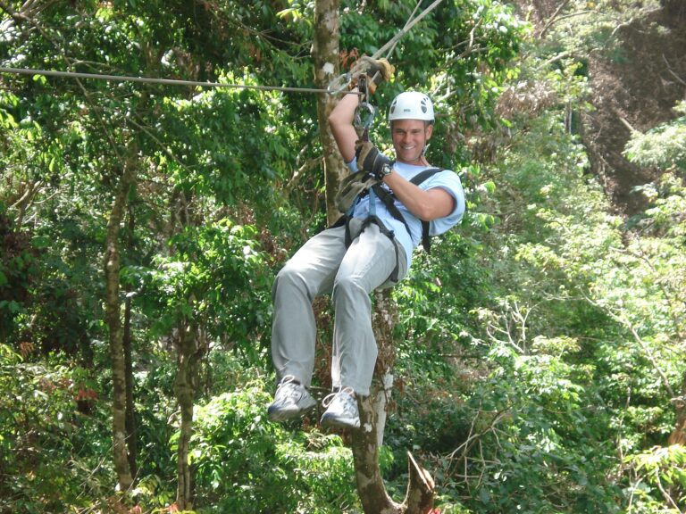 Person gliding along a zip line through a green forest canopy