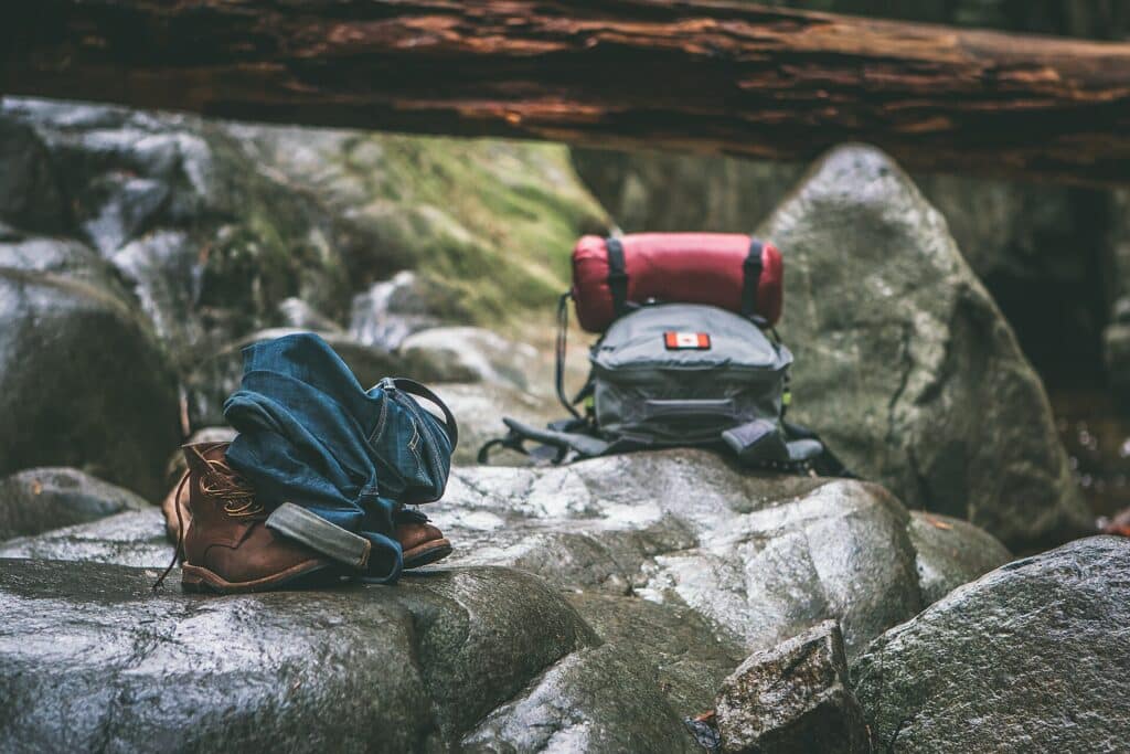 Hiking boots and backpacks resting on rocks beside a forest trail